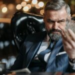 Mature businessman in a suit inspecting a glass of whiskey with focus indoors.